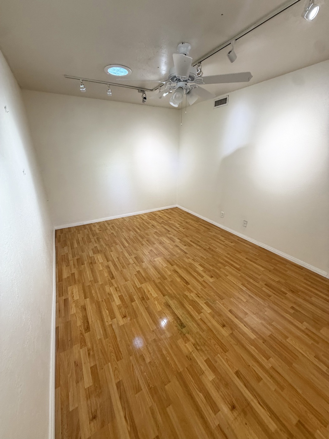 An empty private studio at ArtHatch with track lighting, ceiling fan and wood floor